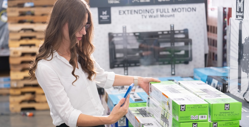 A Sam's Club member uses her phone to more closely inspect a TV wall mount in-club.